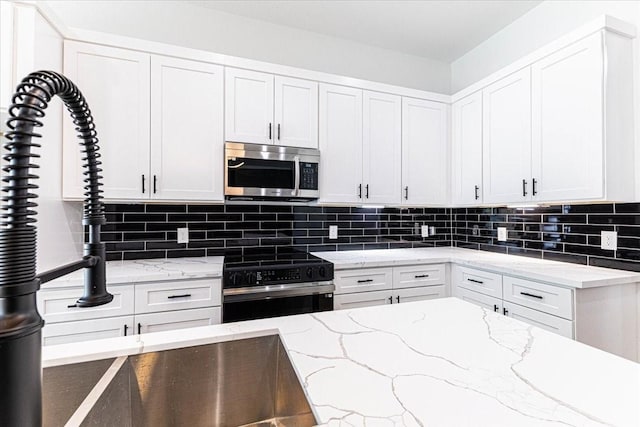 kitchen featuring decorative backsplash, stainless steel microwave, white cabinets, and electric range oven