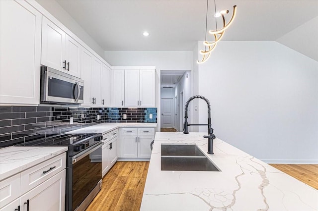 kitchen featuring light wood finished floors, backsplash, appliances with stainless steel finishes, white cabinetry, and a sink