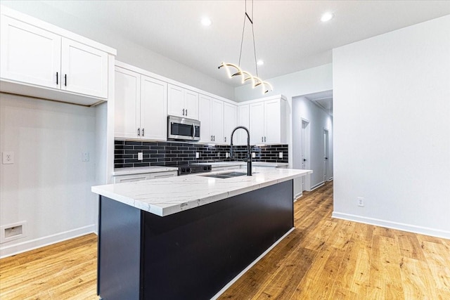 kitchen with light wood finished floors, a sink, white cabinetry, stainless steel microwave, and backsplash