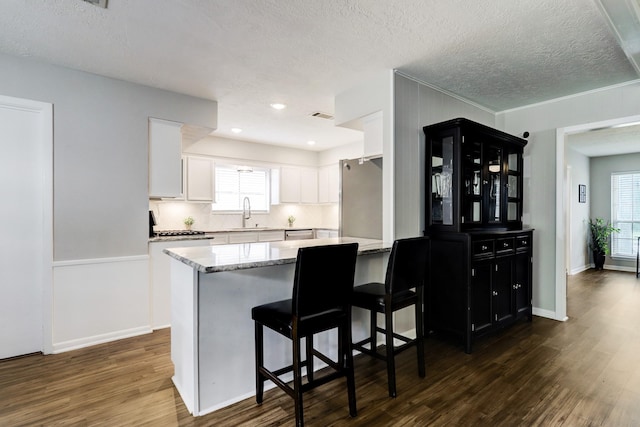 kitchen featuring a peninsula, white cabinetry, freestanding refrigerator, and dark wood-type flooring