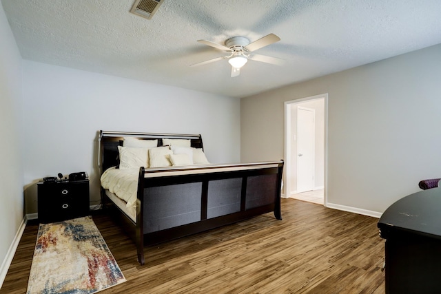 bedroom with visible vents, a textured ceiling, baseboards, and wood finished floors