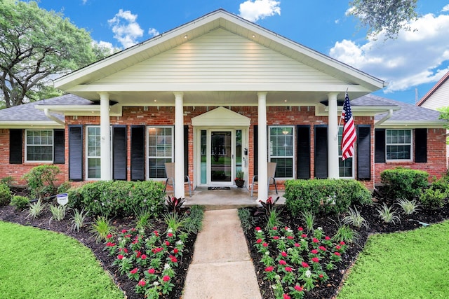 view of front of home with a porch, brick siding, and roof with shingles