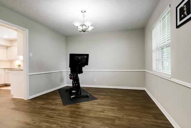 workout room with a chandelier, a textured ceiling, baseboards, and wood finished floors