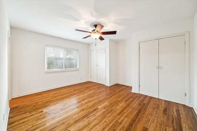 unfurnished bedroom with ceiling fan, baseboards, multiple closets, and wood finished floors