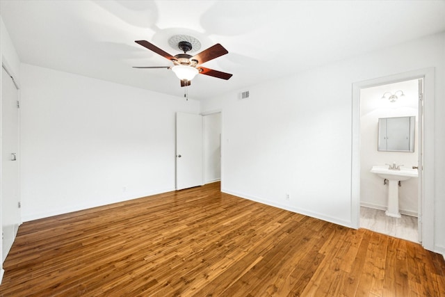 unfurnished bedroom featuring visible vents, ceiling fan, baseboards, ensuite bathroom, and hardwood / wood-style flooring