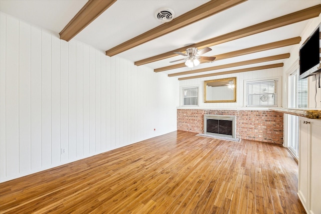 unfurnished living room featuring visible vents, beam ceiling, light wood-style flooring, a ceiling fan, and a brick fireplace