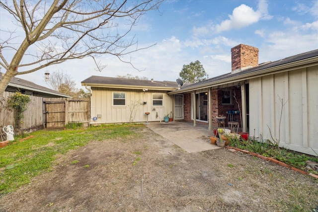 rear view of house featuring a patio, fence, a chimney, board and batten siding, and brick siding