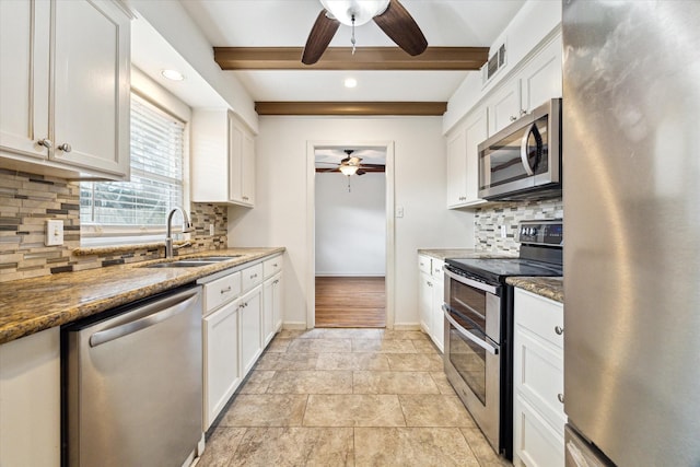 kitchen featuring baseboards, beam ceiling, appliances with stainless steel finishes, white cabinets, and a sink