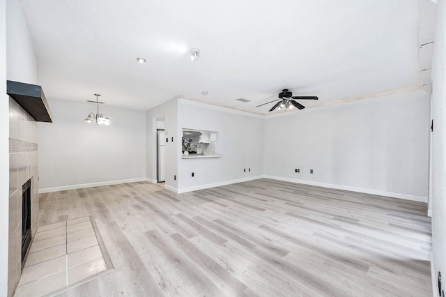 unfurnished living room featuring a tiled fireplace, light wood-style flooring, ceiling fan with notable chandelier, and baseboards