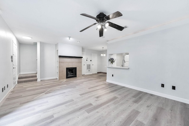 unfurnished living room featuring light wood finished floors, visible vents, baseboards, ceiling fan with notable chandelier, and a tile fireplace