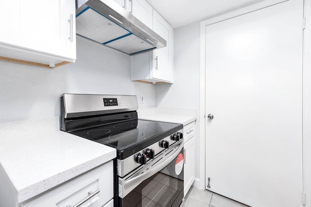 kitchen with light stone countertops, under cabinet range hood, electric stove, light tile patterned flooring, and white cabinets