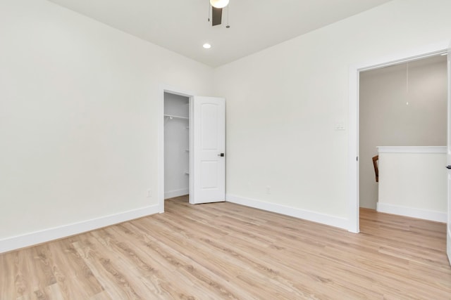 unfurnished bedroom featuring baseboards, attic access, ceiling fan, light wood-style floors, and a closet