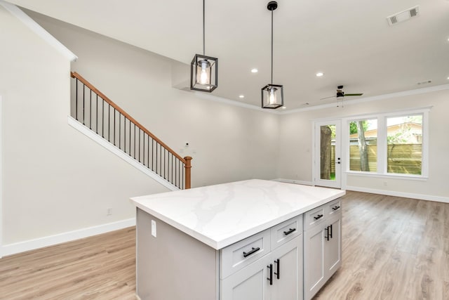 kitchen with visible vents, a kitchen island, baseboards, ornamental molding, and light wood-style flooring