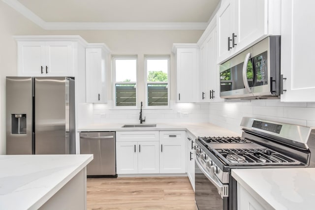 kitchen with a sink, appliances with stainless steel finishes, ornamental molding, and white cabinetry