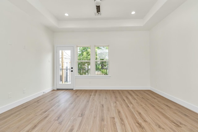 unfurnished room featuring recessed lighting, baseboards, light wood-style floors, and a raised ceiling