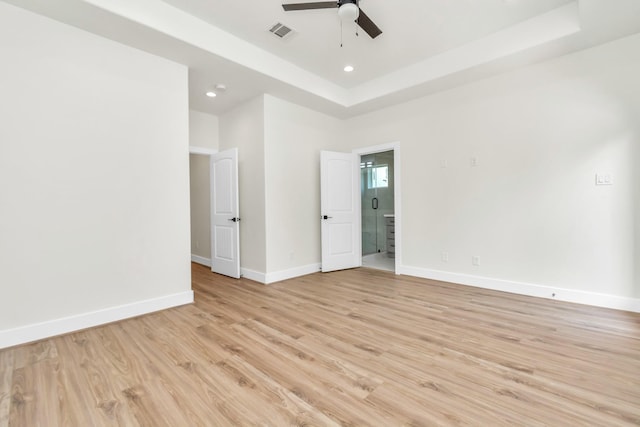 empty room with visible vents, a raised ceiling, light wood-type flooring, and baseboards