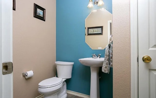 half bathroom with toilet, baseboards, and a sink