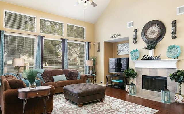 living room featuring wood finished floors, visible vents, high vaulted ceiling, ceiling fan, and a tiled fireplace