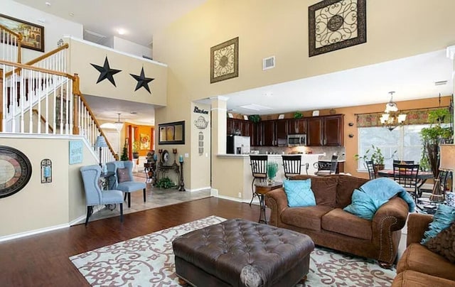 living area with wood finished floors, visible vents, ornate columns, an inviting chandelier, and stairs