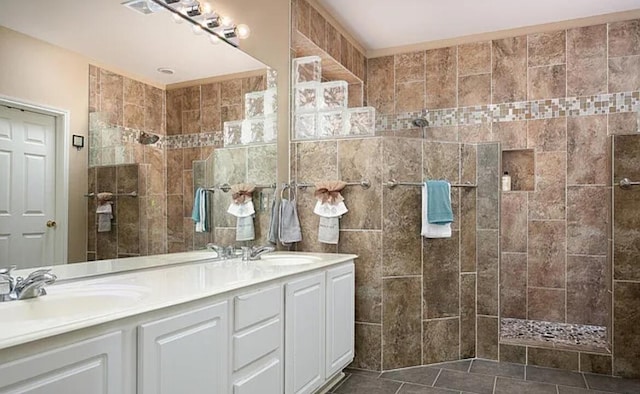 full bath featuring double vanity, tiled shower, tile patterned floors, and a sink