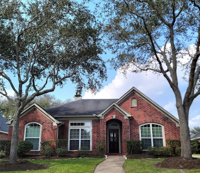 view of front of home with brick siding, a chimney, a front yard, and roof with shingles