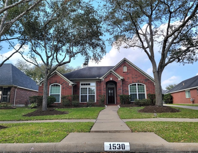 traditional home with brick siding, a chimney, a front yard, and roof with shingles