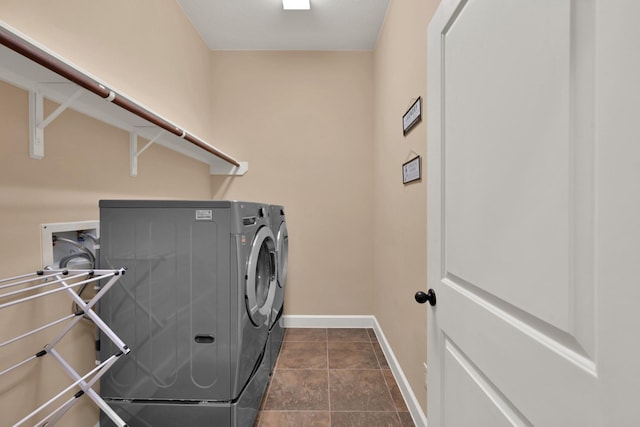 clothes washing area featuring dark tile patterned floors, laundry area, washer and dryer, and baseboards