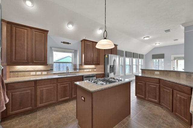 kitchen featuring light stone counters, lofted ceiling, a sink, appliances with stainless steel finishes, and backsplash