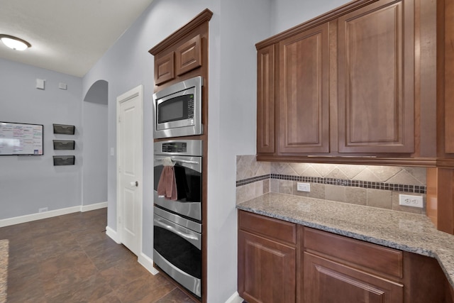 kitchen with arched walkways, appliances with stainless steel finishes, tasteful backsplash, and light stone counters