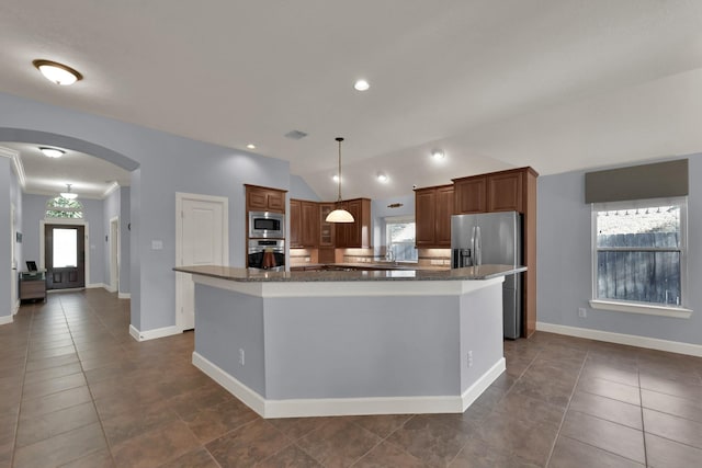 kitchen with a spacious island, vaulted ceiling, dark stone countertops, appliances with stainless steel finishes, and arched walkways