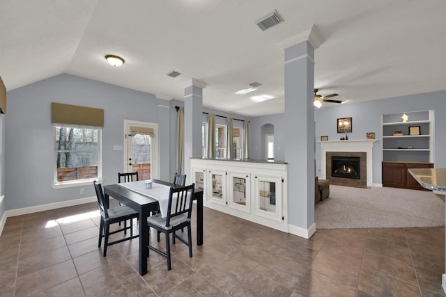 dining room with built in features, visible vents, a ceiling fan, and a tile fireplace