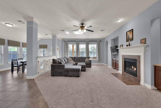 carpeted living room with a ceiling fan, baseboards, ornate columns, tile patterned flooring, and a tiled fireplace