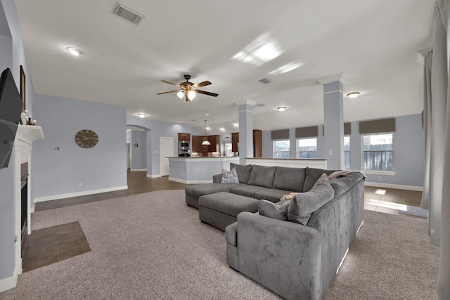 living area with visible vents, ornate columns, dark tile patterned flooring, a fireplace with flush hearth, and ceiling fan