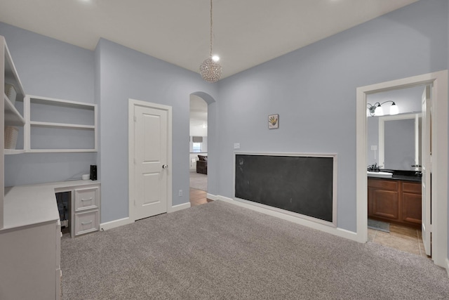 interior space featuring arched walkways, light colored carpet, baseboards, and a sink