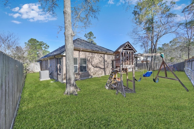 back of property with a fenced backyard, a playground, central air condition unit, a lawn, and brick siding