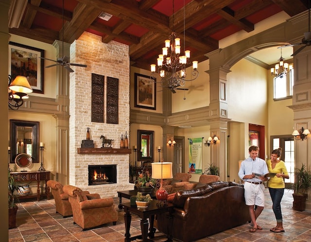 living room with visible vents, coffered ceiling, beam ceiling, a brick fireplace, and ceiling fan with notable chandelier