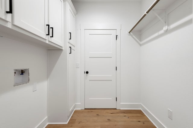 clothes washing area featuring washer hookup, cabinet space, baseboards, and light wood finished floors