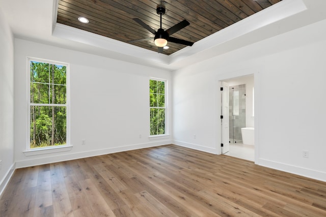 spare room with a tray ceiling, wood finished floors, baseboards, and wooden ceiling