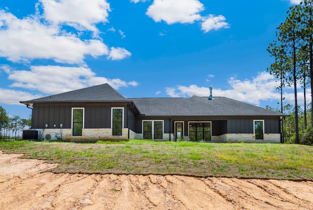 back of property featuring central air condition unit, stone siding, board and batten siding, and a shingled roof