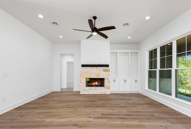 unfurnished living room with a stone fireplace, recessed lighting, wood finished floors, and visible vents