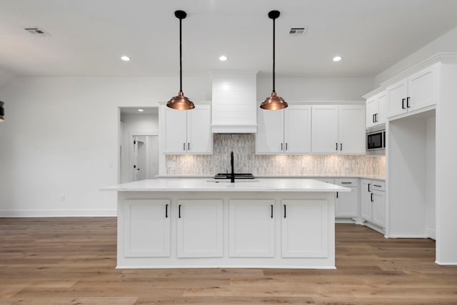 kitchen featuring decorative backsplash, stainless steel microwave, custom range hood, and light countertops