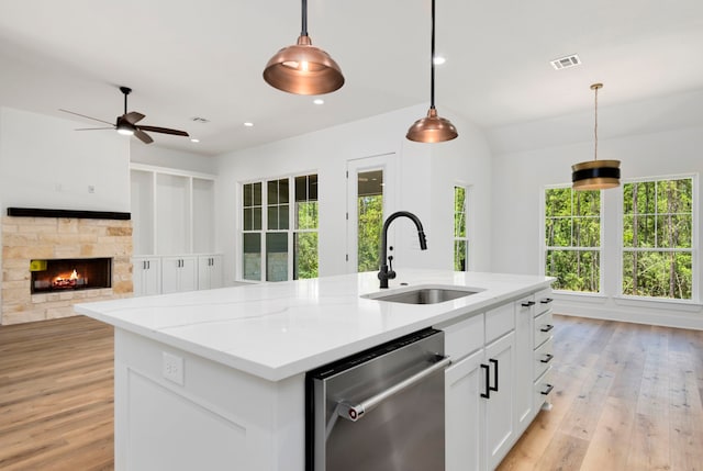 kitchen featuring pendant lighting, dishwasher, a stone fireplace, white cabinetry, and a sink