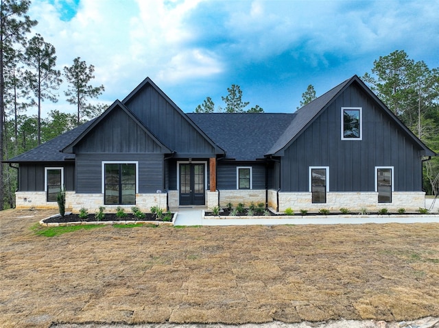 view of front of home with board and batten siding, a shingled roof, a front lawn, french doors, and stone siding