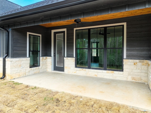 doorway to property with stone siding, roof with shingles, and a ceiling fan