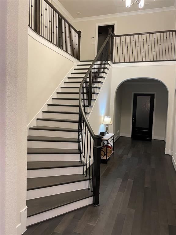 staircase featuring wood finished floors, baseboards, a high ceiling, arched walkways, and ornamental molding