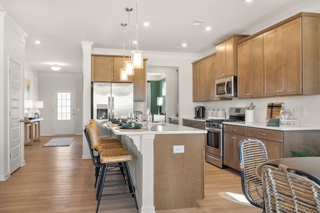 kitchen featuring light wood-style flooring, a kitchen island with sink, ornamental molding, appliances with stainless steel finishes, and a kitchen breakfast bar