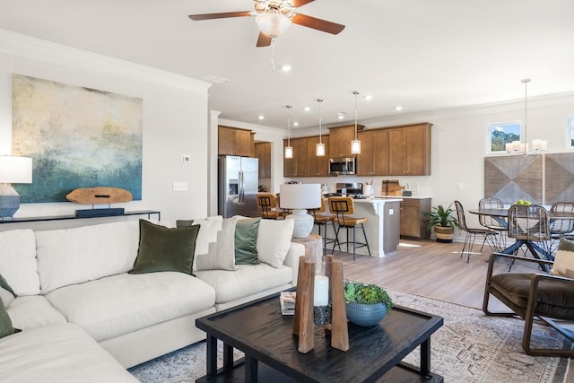 living room featuring light wood finished floors, crown molding, baseboards, recessed lighting, and ceiling fan with notable chandelier