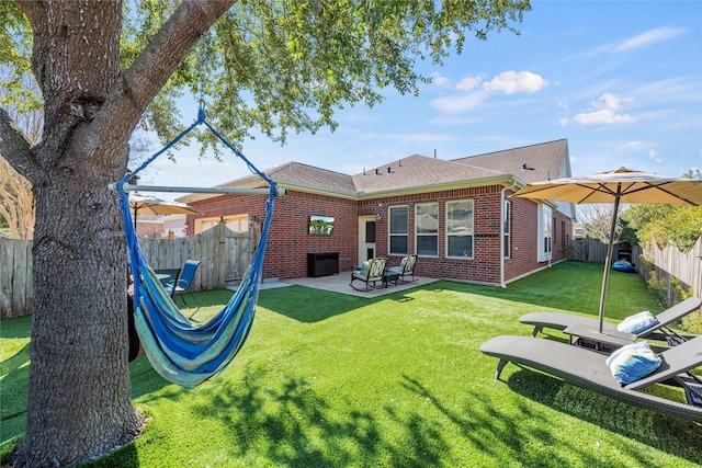 back of house with a fenced backyard, a yard, roof with shingles, brick siding, and a patio area