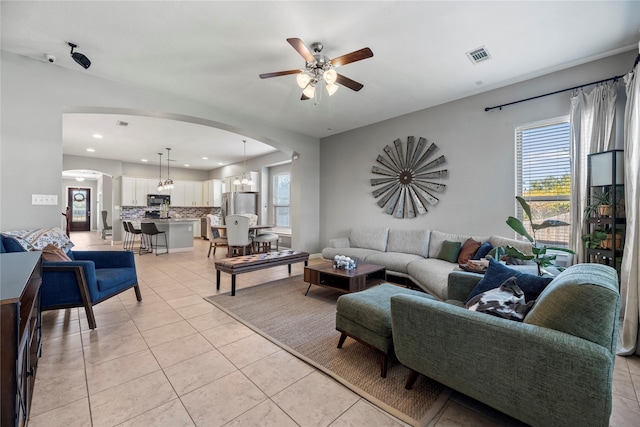 living room with light tile patterned floors, visible vents, arched walkways, and a wealth of natural light