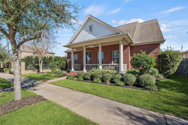 view of front of home with a front lawn, fence, covered porch, and brick siding